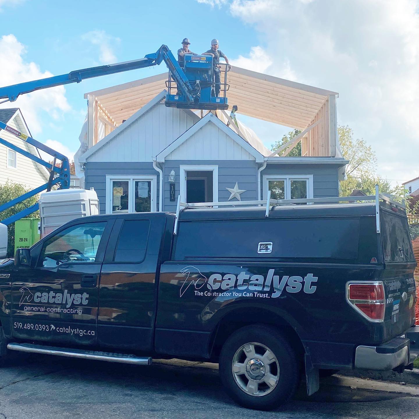 Two Catalyst contractors in a cherry picker in front of a home that's being renovated.